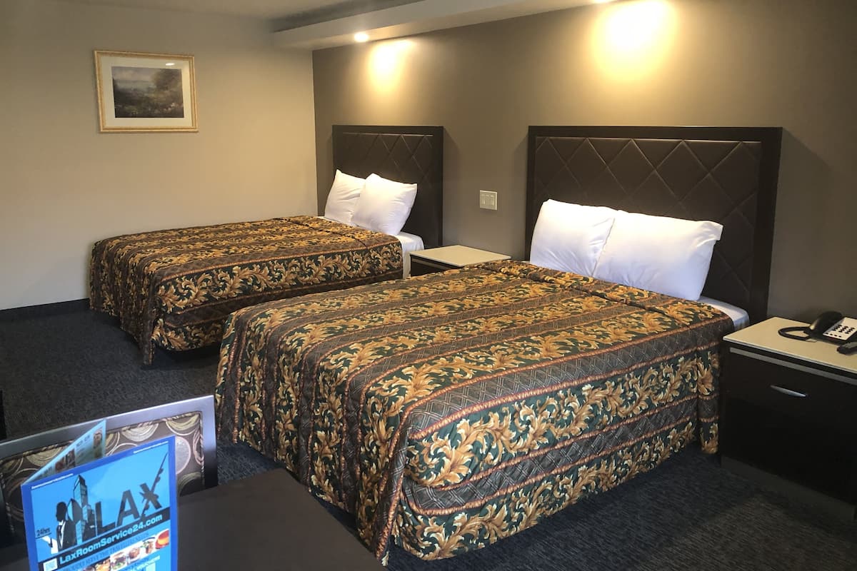 A hotel room with two beds, each with a patterned bedspread, a nightstand with a phone, and a framed picture on the wall.