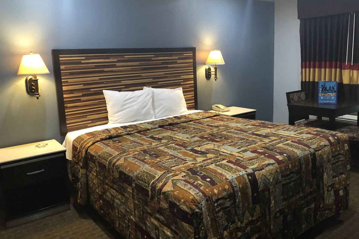 A hotel room with a large bed, two bedside lamps, a nightstand with a telephone, and a small table with a sign.
