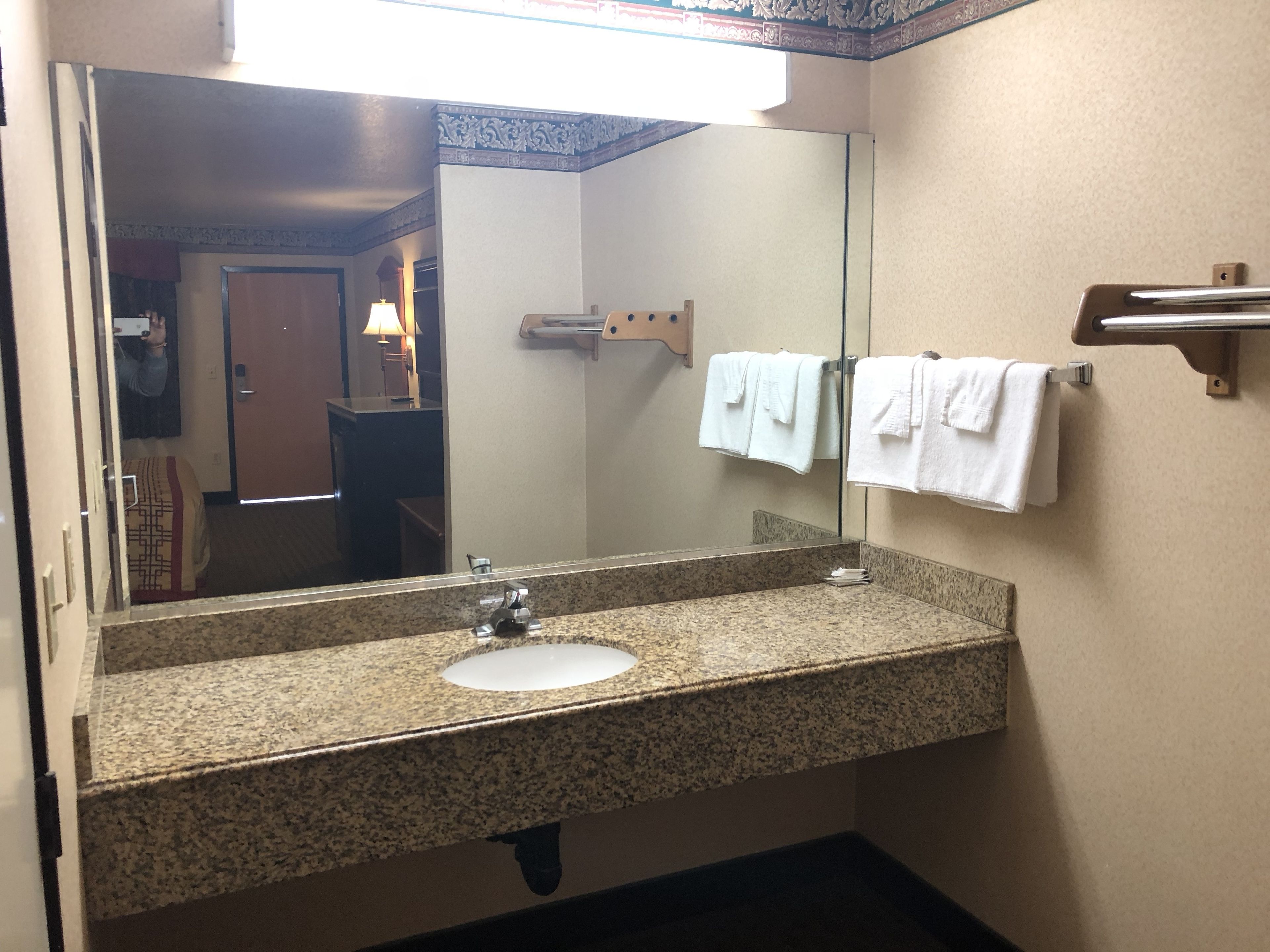 A bathroom with a granite countertop sink, a mirror, and a towel rack with white towels.