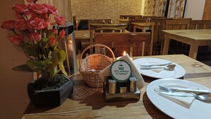 A dining table set with a candle, a bottle of Shandela Hotel, and a potted plant. - CS Shhandella Hotel (Manali)