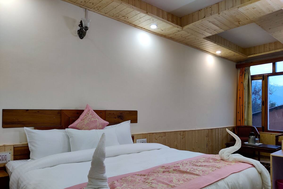A neatly made bed with a wooden headboard, a bedside table with a lamp, and a window with curtains.