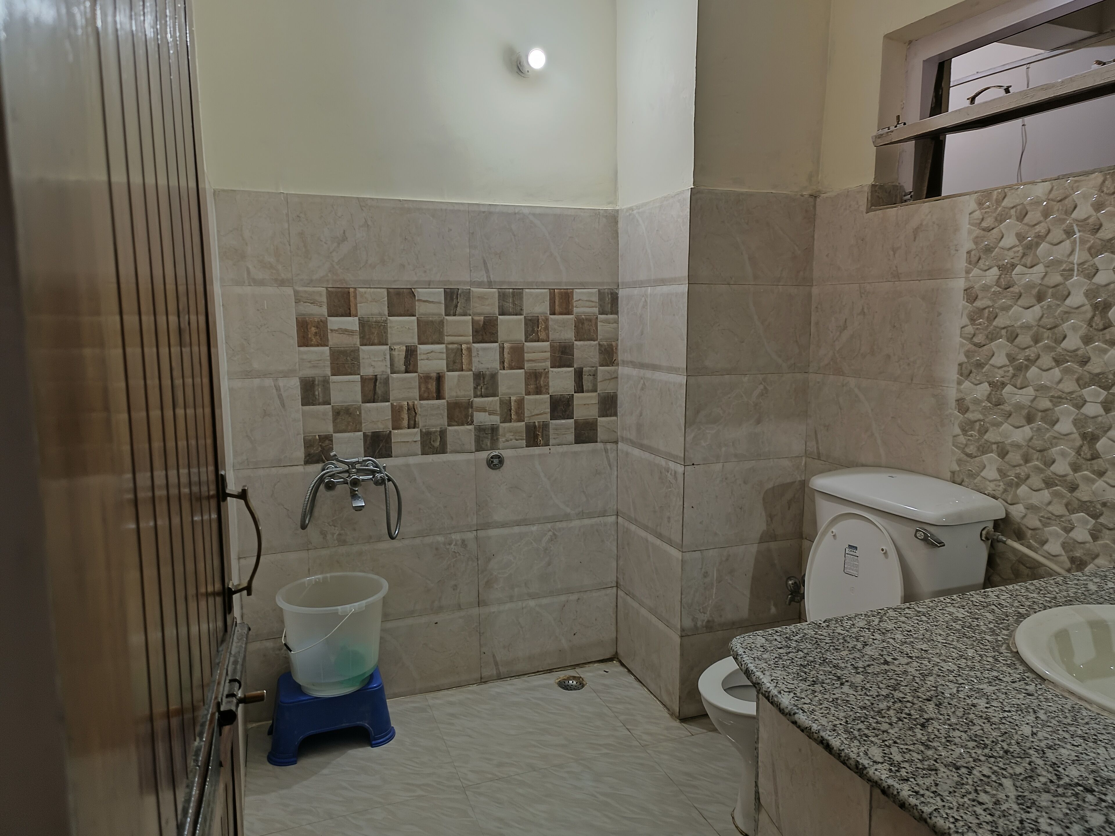 A bathroom with a tiled shower wall, a toilet, and a sink with a granite countertop.