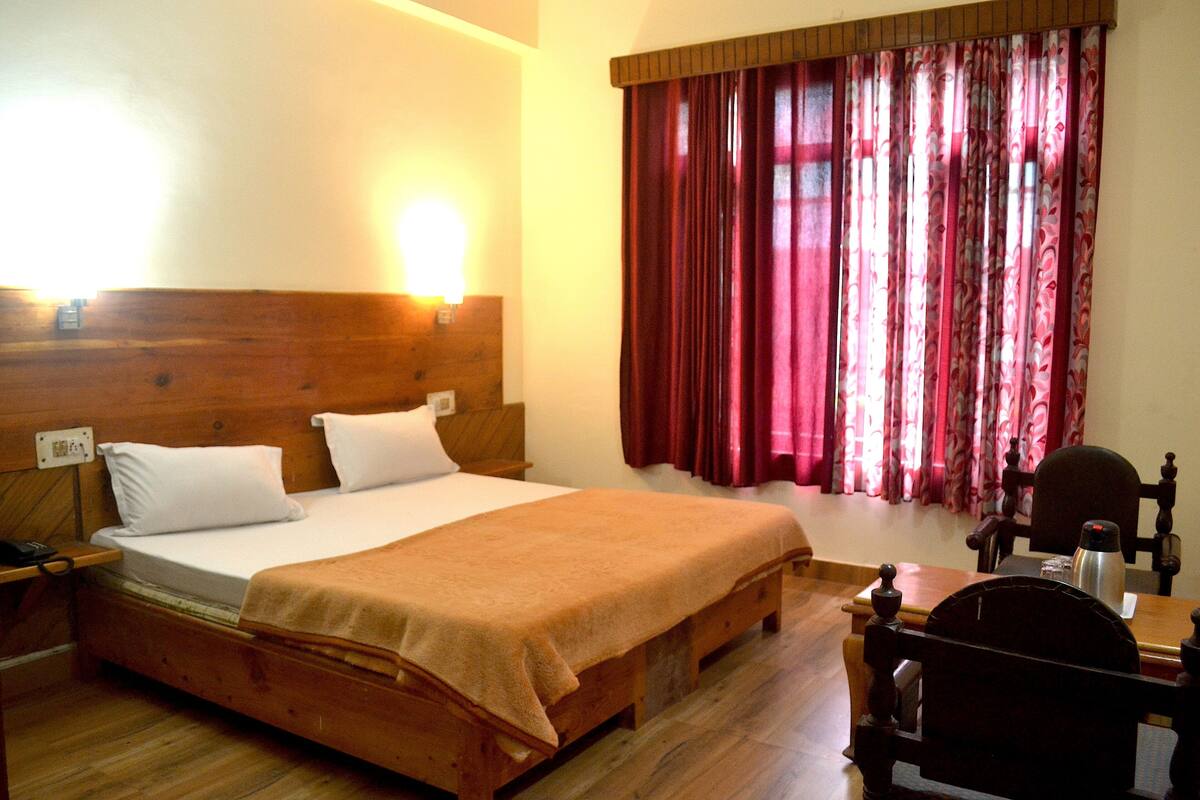 A wooden bed with a headboard, a bedside table with a lamp, and a window with red curtains.