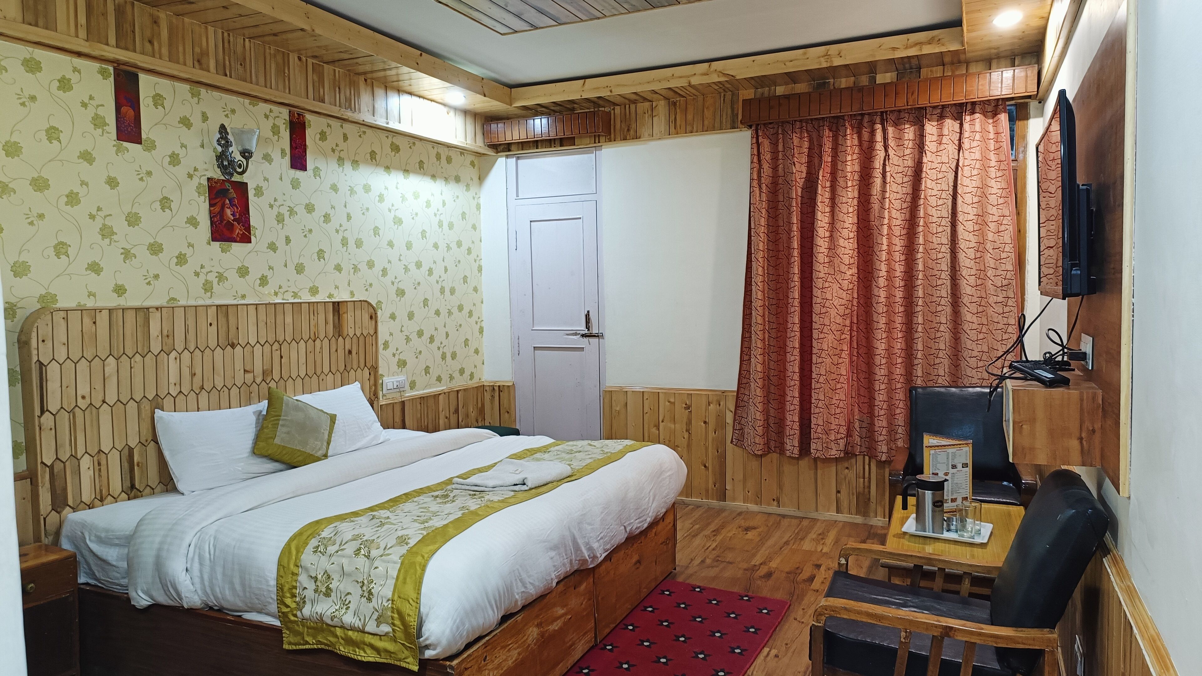 Una habitación con una cama de cabecera de madera, un escritorio con silla, un televisor y una puerta.