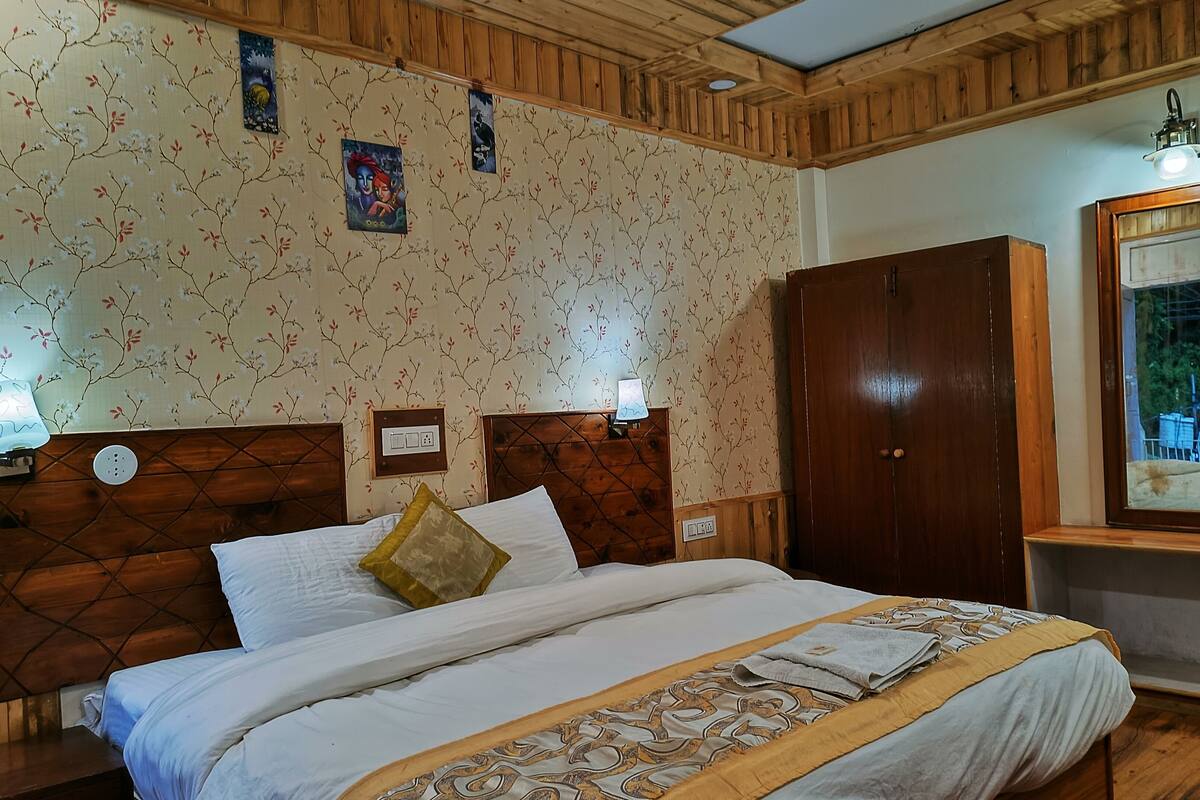 A bedroom with a wooden headboard, a bed with white linens, a wooden wardrobe, and a mirror with a view of the outdoors.
