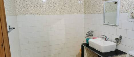 Un baño con paredes de azulejos blancos, una encimera negra y un espejo sobre el lavabo.