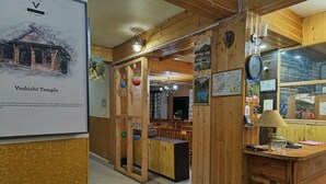 A wooden interior with a travel desk, a clock, and a poster of Vashisht Temple. - CS Shhandella Hotel (Manali)