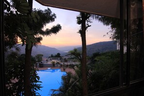 A view of a swimming pool surrounded by lush greenery and a mountainous landscape during sunset. - Mount View Executive  The Valley Resort (Jaoli)