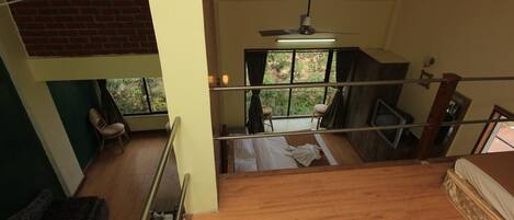 Habitación con piso de madera, una cama, ventilador de techo y vistas al exterior a través de una ventana.