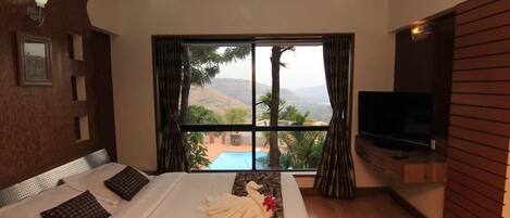 Une chambre d’hôtel avec un grand lit, une télévision et une vue sur une piscine et des montagnes.