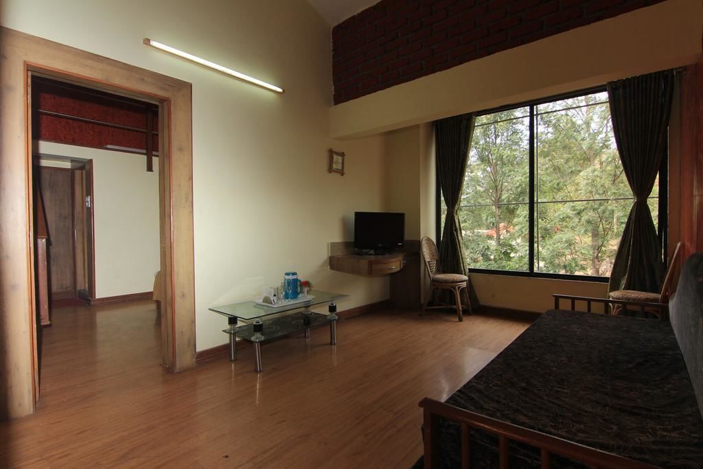 A room with a bed, a TV, a glass table, and a window with curtains.