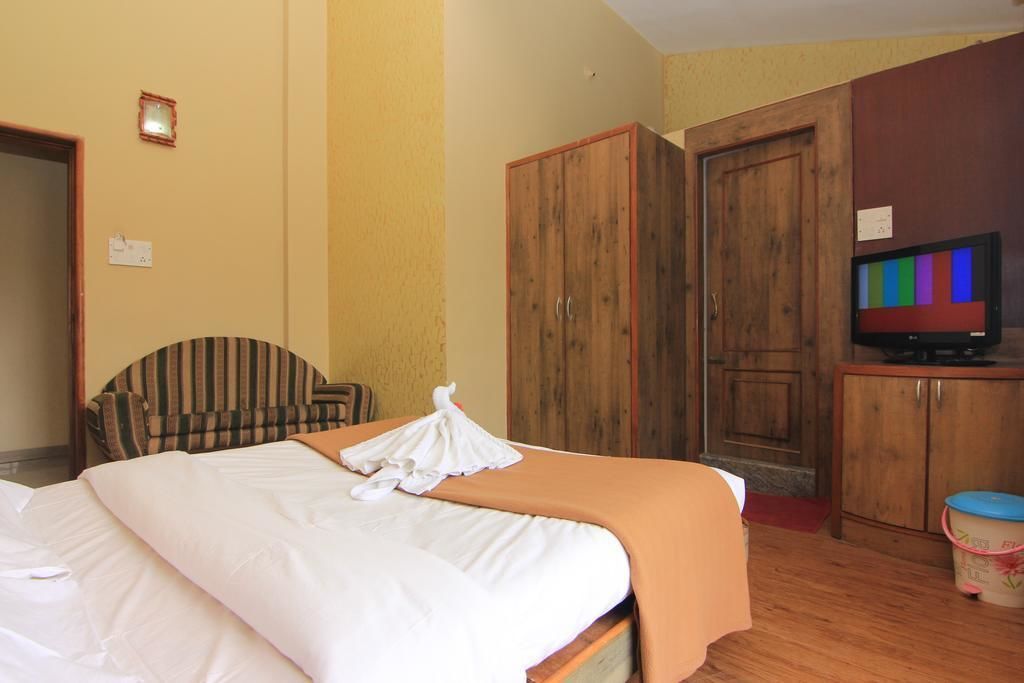 A hotel room with a bed, a wooden wardrobe, a television, and a chair.