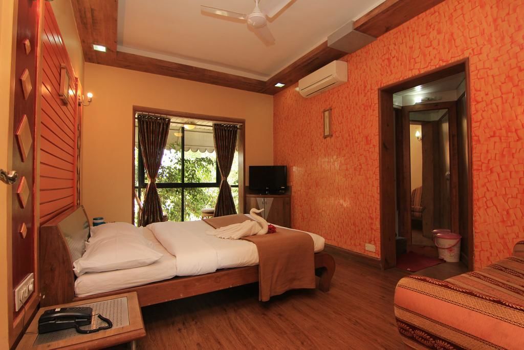 A hotel room with a bed, a television, a desk with a telephone, and a window with curtains.