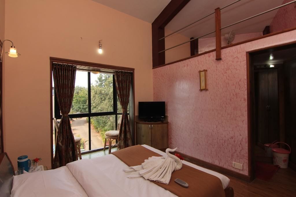 A hotel room with a bed, a television on a stand, a window with curtains, and a door.