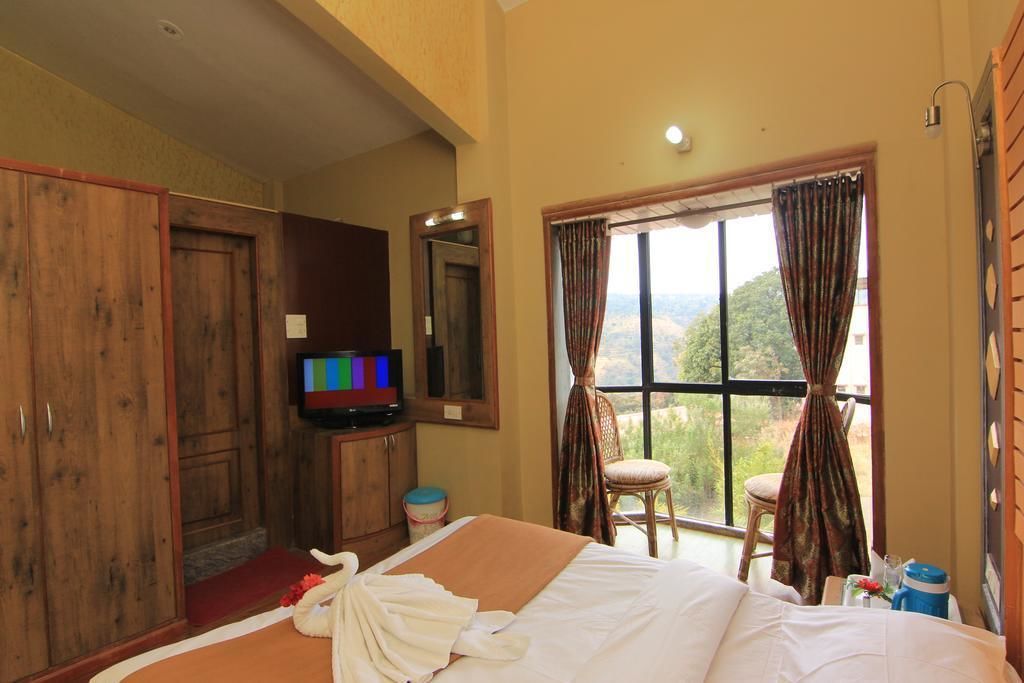 Habitación de hotel con cama, televisor, ventana con cortinas y vistas al exterior.