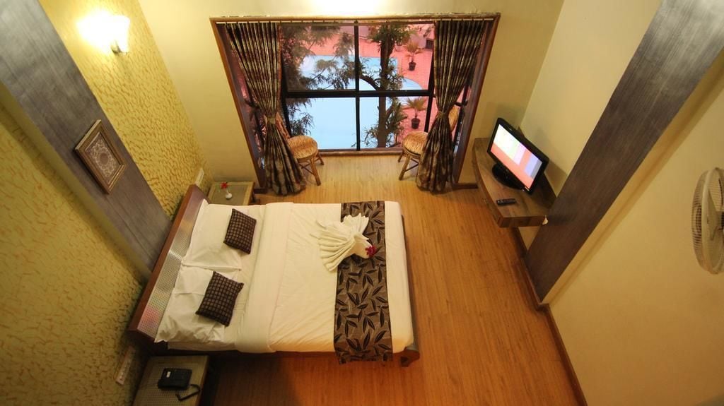A hotel room with a bed, a desk with a computer, a TV, and a window with curtains.