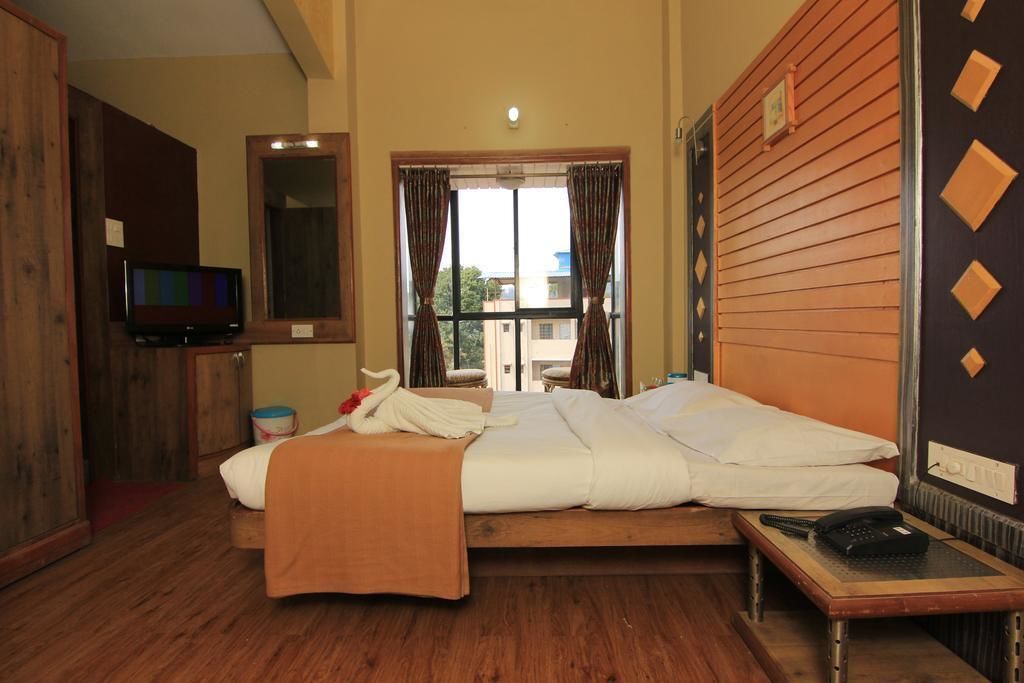 A hotel room with a bed, a television, a window with curtains, and a wooden wall.