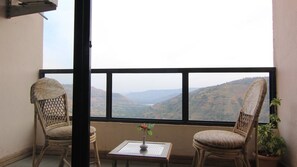 A balcony with wicker chairs and a small table with a vase of flowers, overlooking a mountainous landscape.