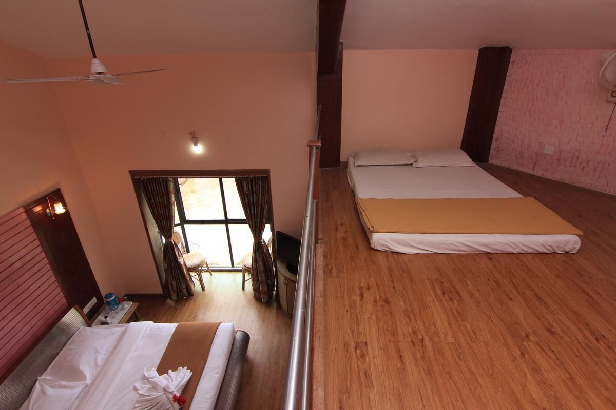 A hotel room with two beds, a ceiling fan, a window with curtains, and a wooden floor.
