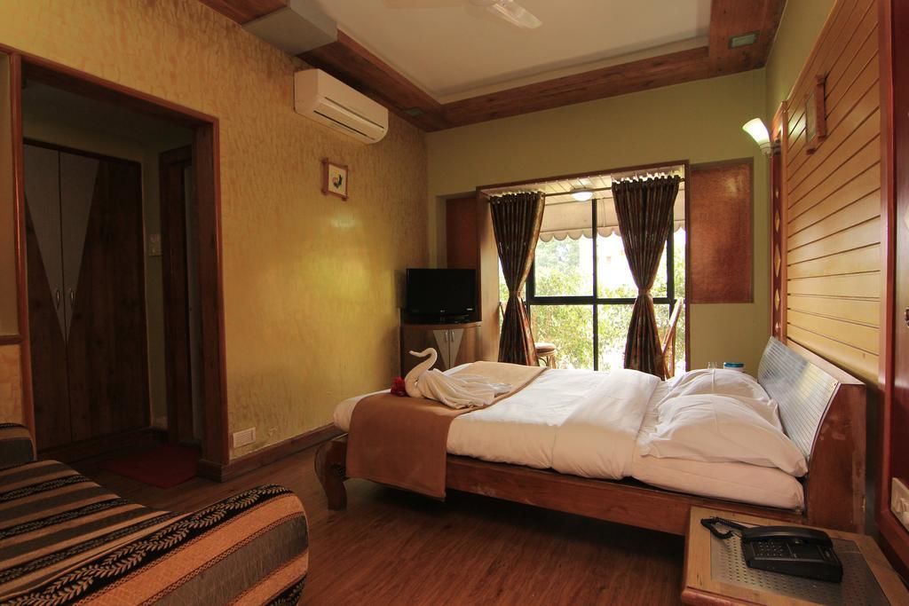 A hotel room with a wooden bed, a television, and a window with curtains.