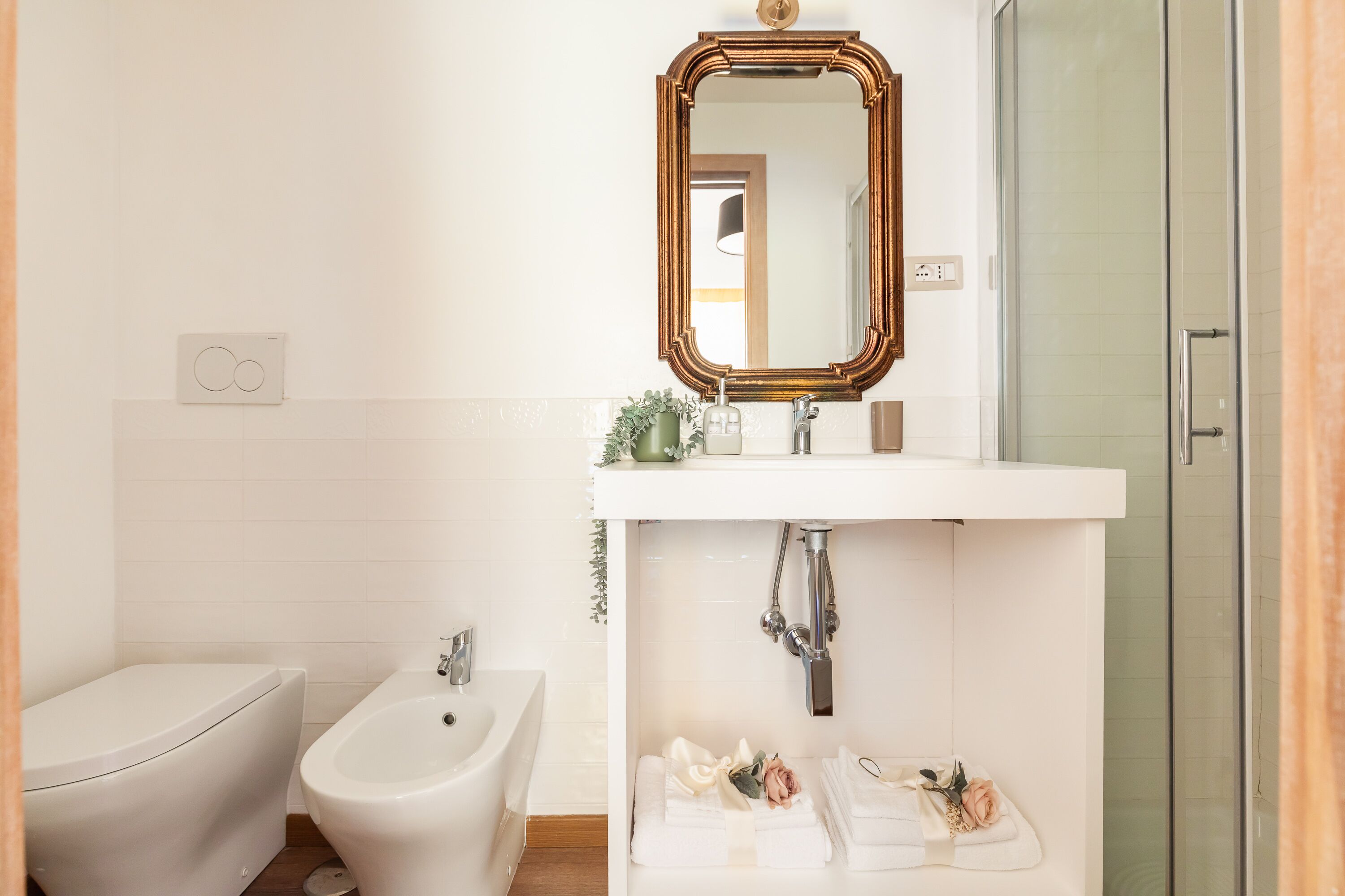 A bathroom with a white sink, a mirror, a bidet, and a shower.