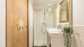 Un baño con cabina de ducha de vidrio, un lavabo con espejo y una puerta de madera con pomo decorativo.