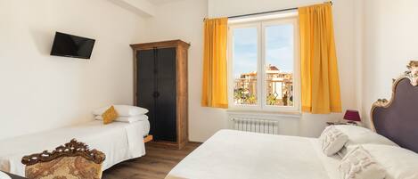 A hotel room with two beds, a TV, a wooden wardrobe, and a window with curtains.