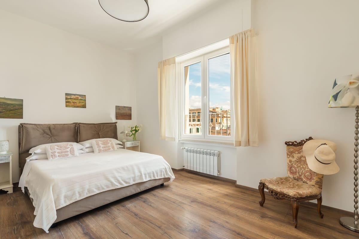 A bedroom with a large bed, a chair, a nightstand, and a window with curtains.