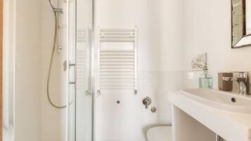 Een badkamer met een douchecabine van glas, een witte wastafel en een toilet.