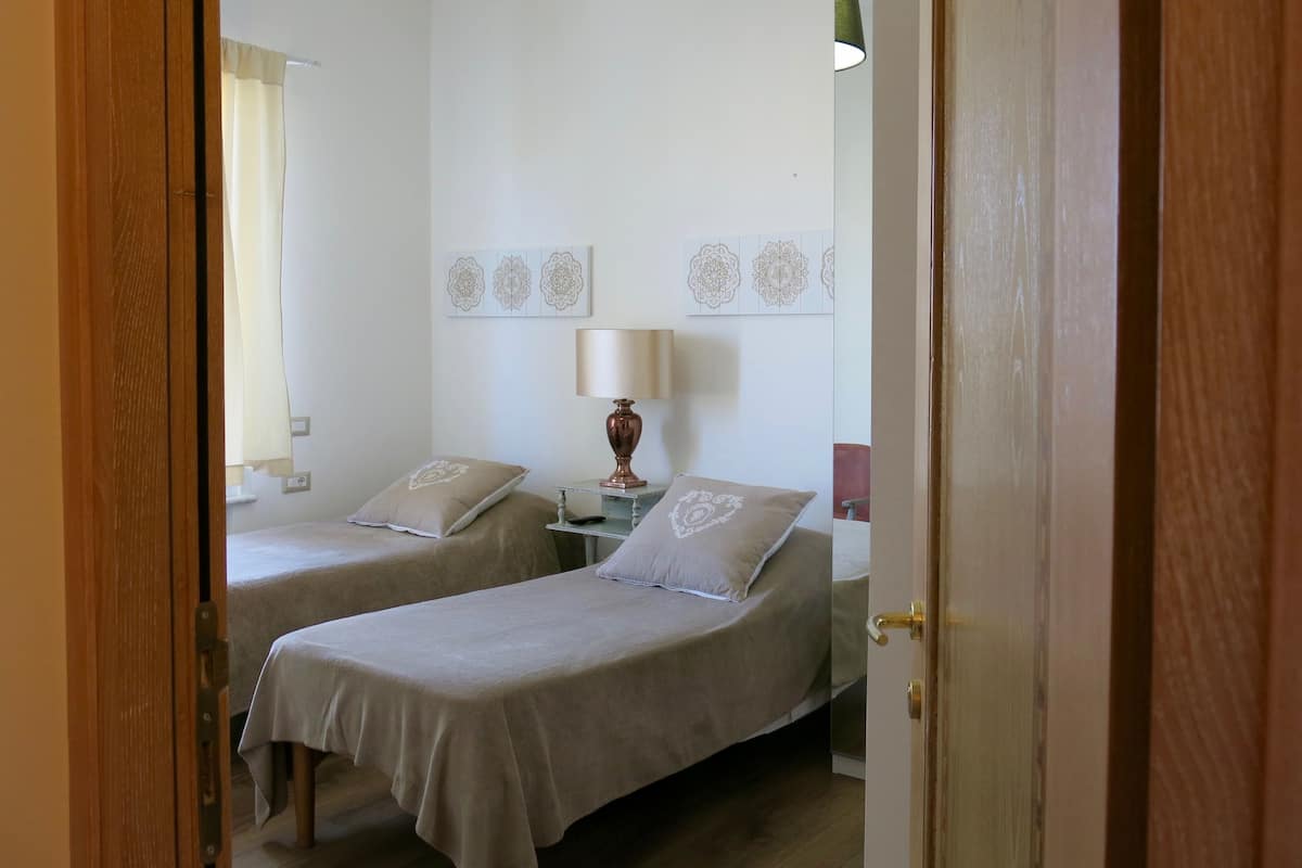 A room with two beds, a bedside table with a lamp, and decorative wall art.