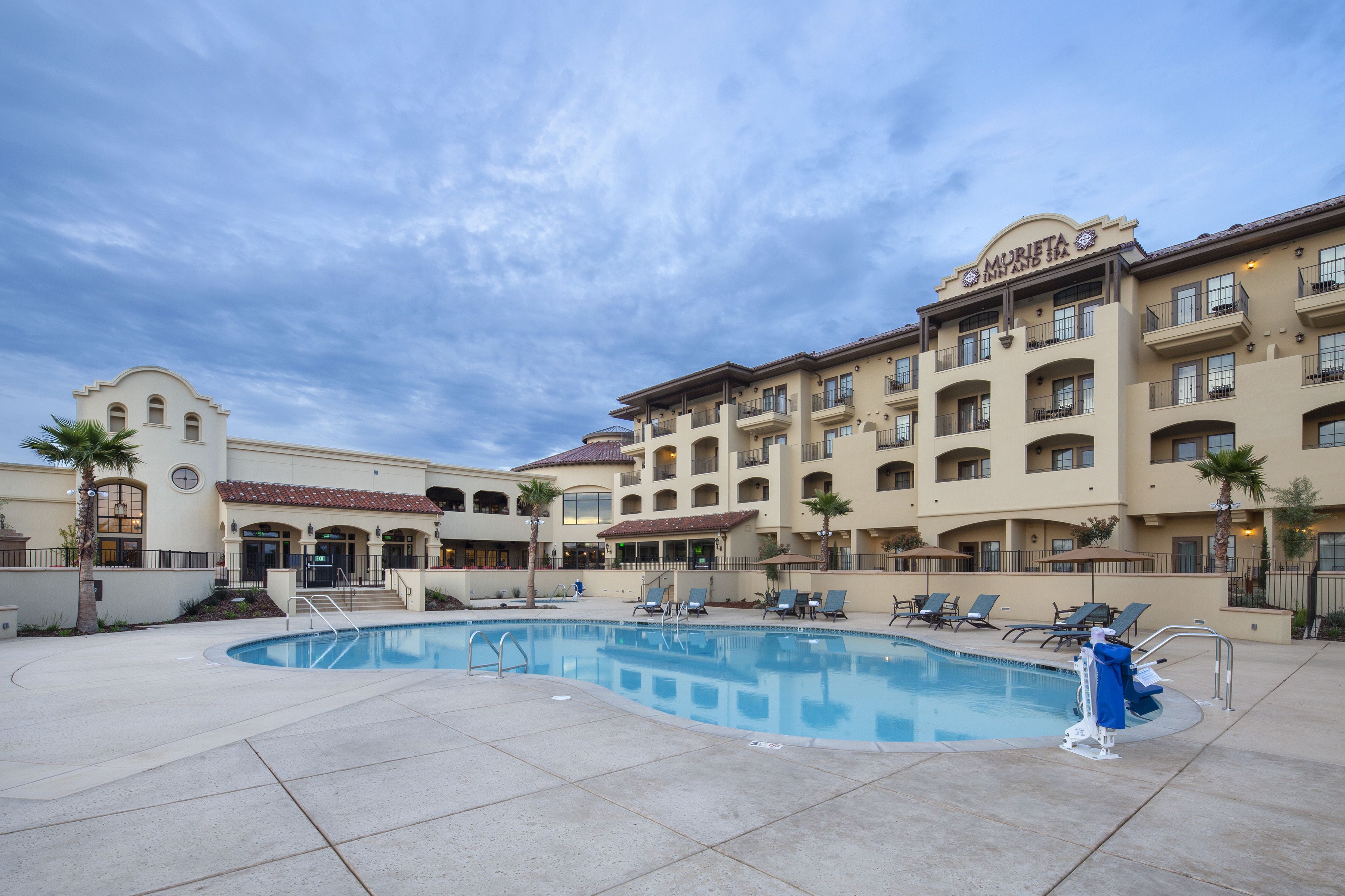 A hotel with a swimming pool, multiple balconies, and a clear sky.