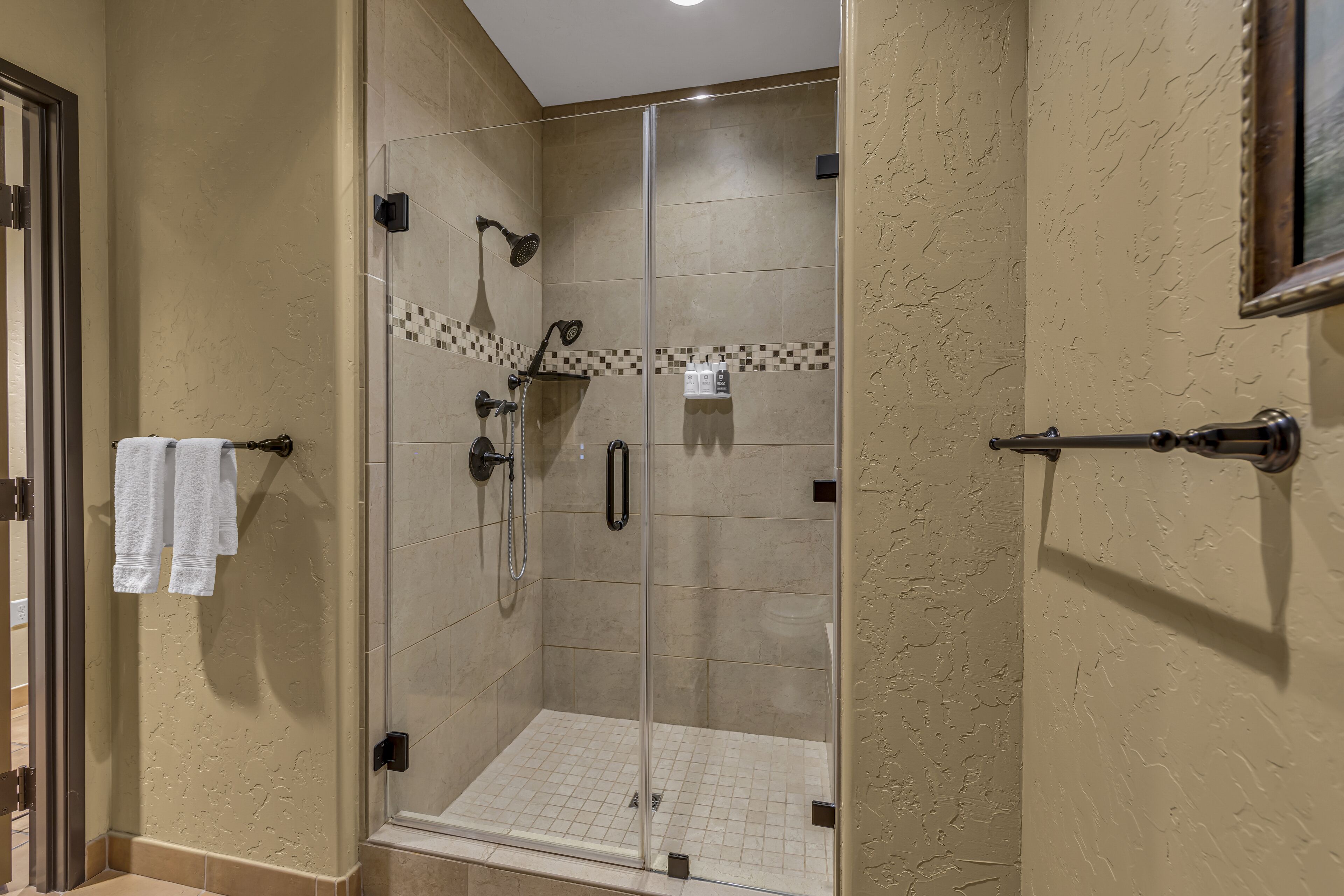A glass-enclosed shower with a tiled floor, a handheld showerhead, and a wall-mounted control panel.