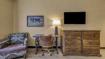 Una habitación con un sillón estampado, un escritorio con lámpara, un aparador de madera y un cuadro en la pared.