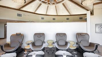 A modern reception area with a curved ceiling, chandeliers, and a row of massage chairs.