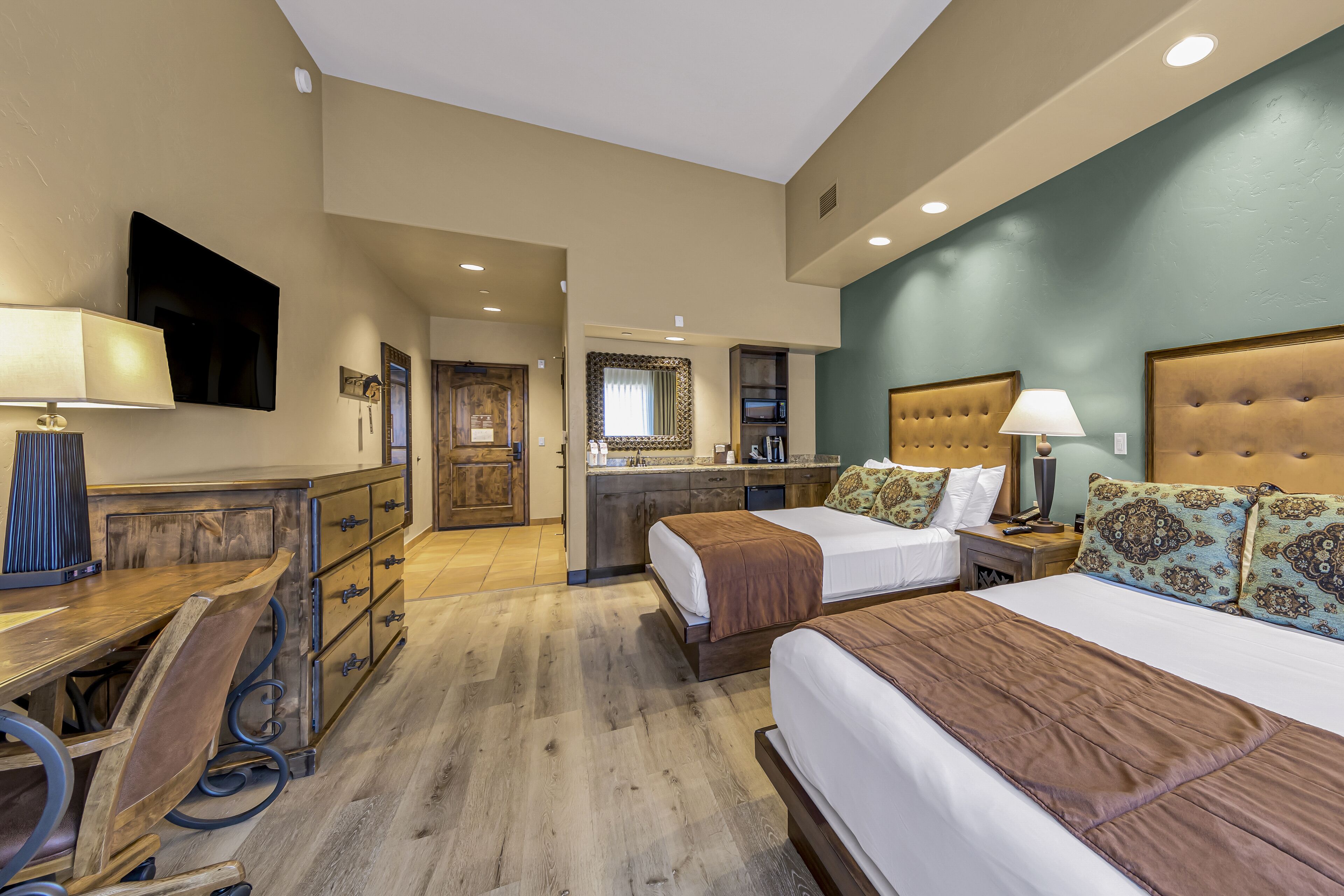 Une chambre d’hôtel avec deux lits, un bureau, une commode, une télévision et une kitchenette.