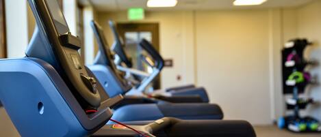 A row of exercise machines in a gym with a ceiling light and a door in the background.