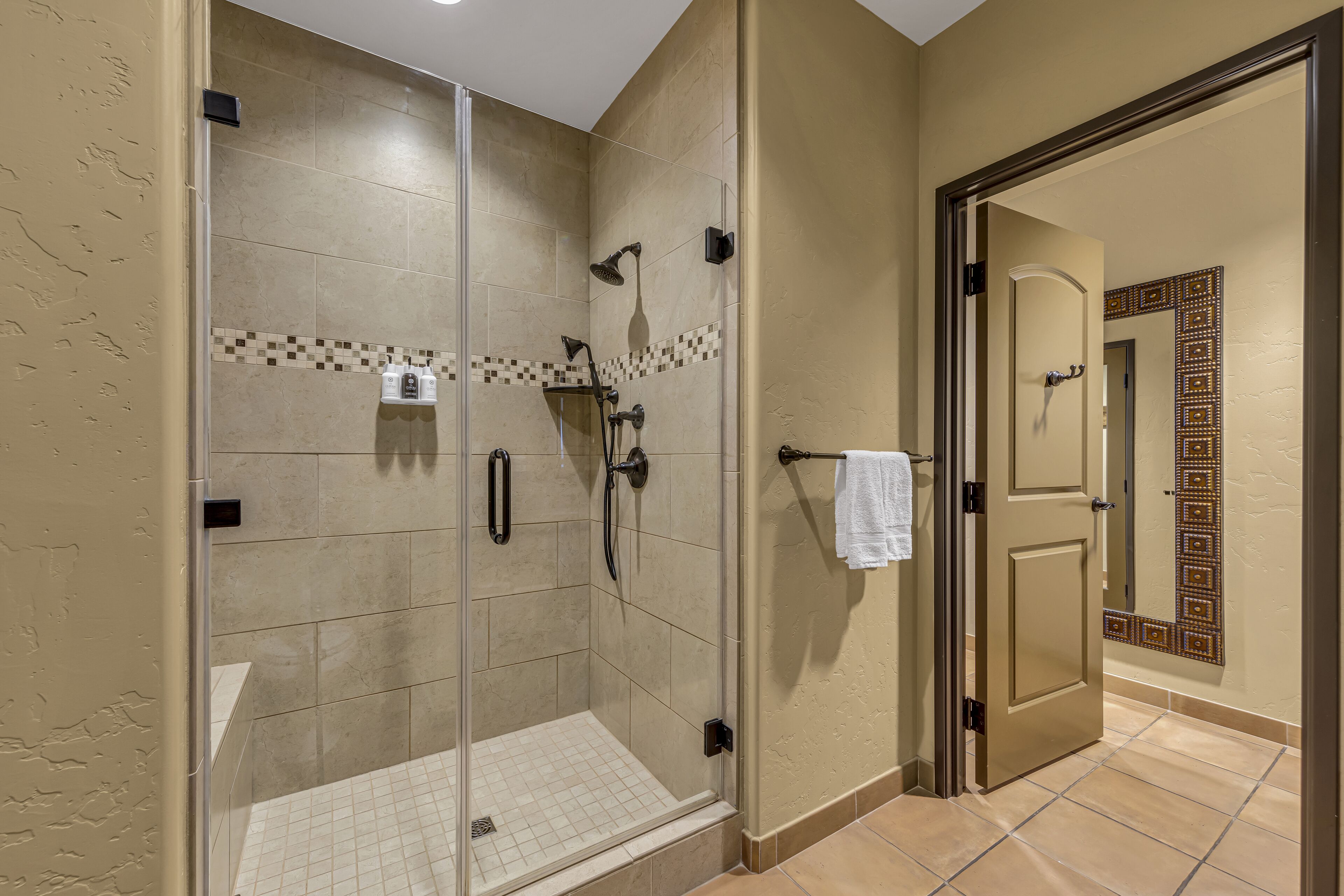 Un baño moderno con cabina de ducha de vidrio, baldosas color beige y un borde decorativo de azulejos.