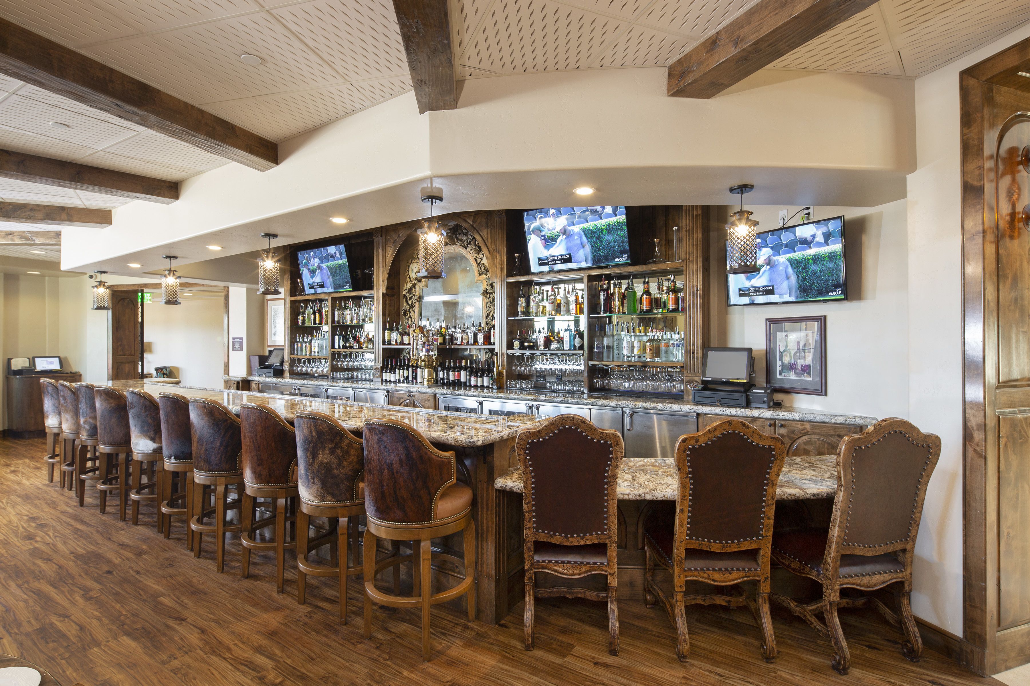 Zona de bar con taburetes de madera, una barra larga y varios televisores montados en la pared.