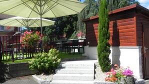 Un edificio de madera con techo rojo, una escalera de piedra y un jardín con flores y arbustos.