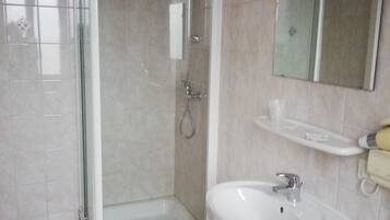 A bathroom with a glass-enclosed shower, a sink with a mirror above it, and a small white trash bin.