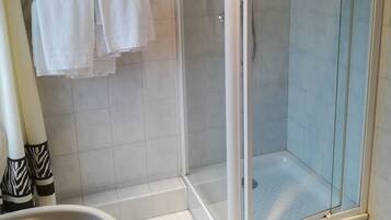A modern bathroom with a glass-enclosed shower, a white sink, and two white towels hanging on a rack.