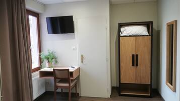 A room with a desk, chair, wardrobe, and a TV mounted on the wall.