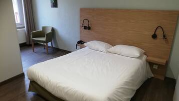 Una habitación de hotel con una cama grande, una silla, una mesita de noche y una lámpara de pared.