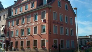 A multi-story building with the sign "HOTEL MOSCHENROSS RESTAURANT" indicating it is a hotel and restaurant.