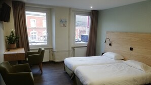 Habitación de hotel con una cama grande, dos sillas, un escritorio y una ventana con vistas a un edificio.