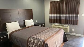 A hotel room with a large bed, a headboard, a nightstand, a window with curtains, and an air conditioning unit.
