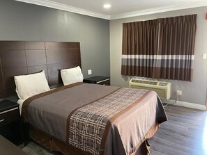 Una habitación de hotel con una cama grande, cabecera, mesita de noche, ventana con cortinas y un equipo de aire acondicionado.