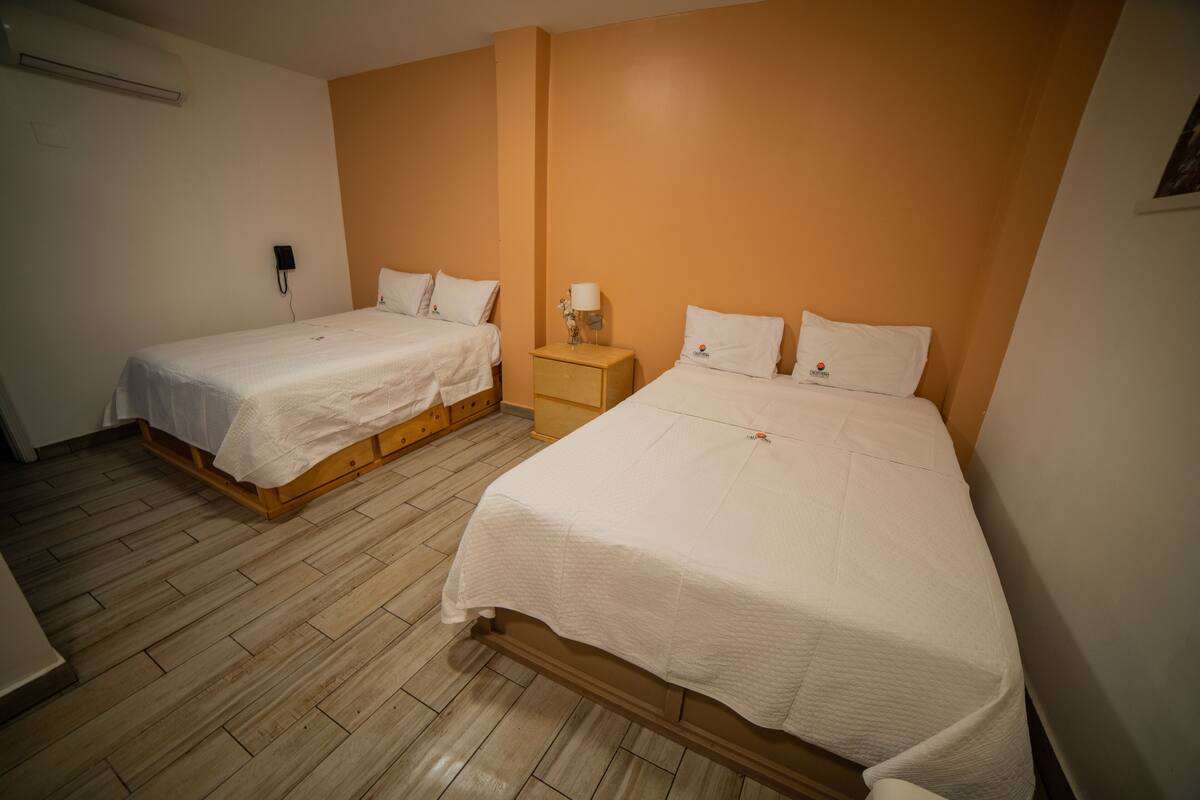A hotel room with two single beds, a bedside table with a lamp, and a phone on the wall.