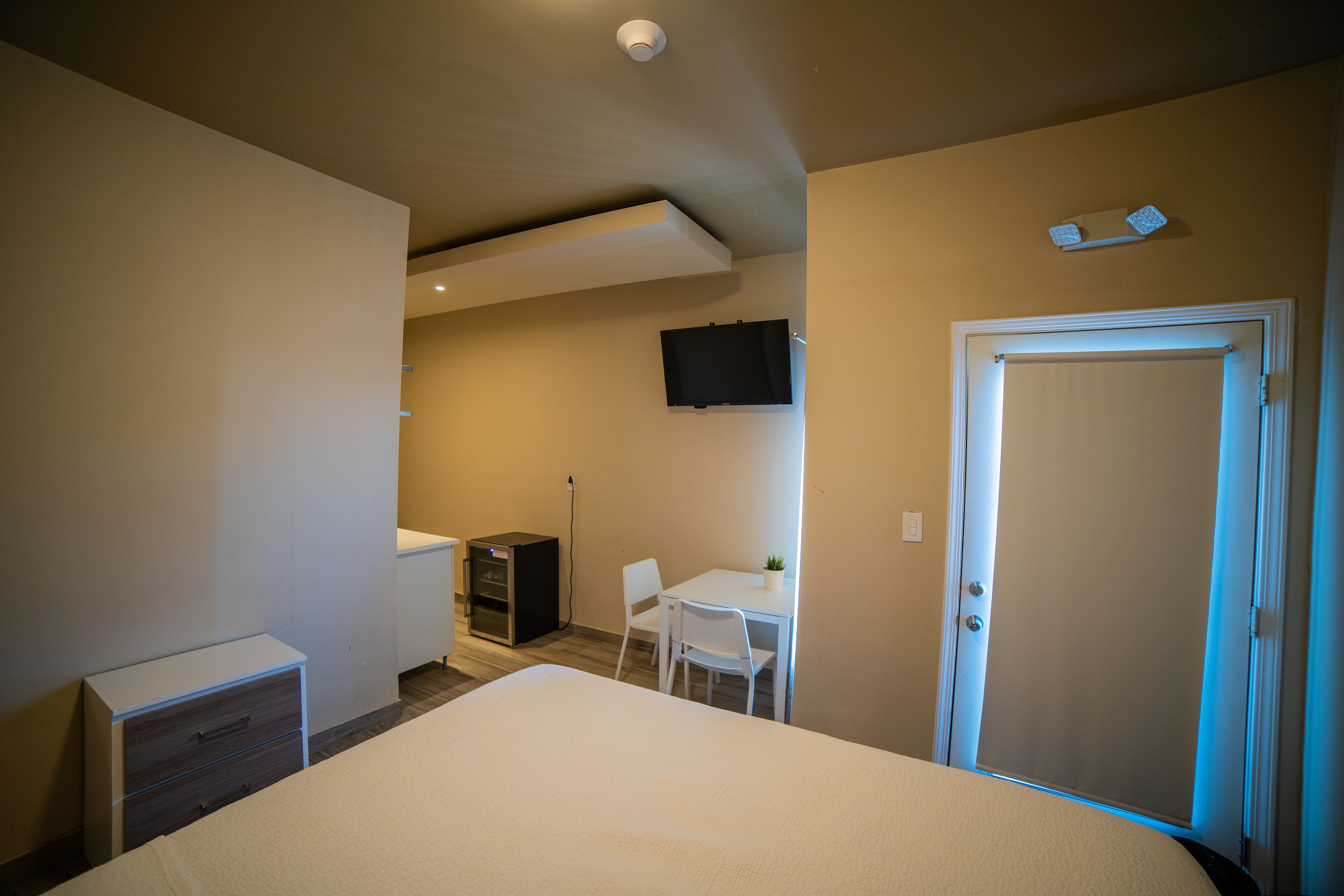 A bedroom with a bed, a desk, a chair, a TV, and a door.