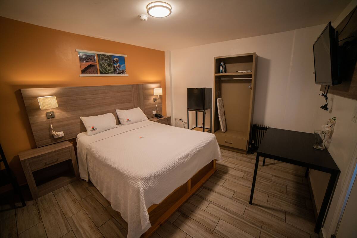 A hotel room with a large bed, bedside tables with lamps, a wardrobe, a desk, and a television mounted on the wall.